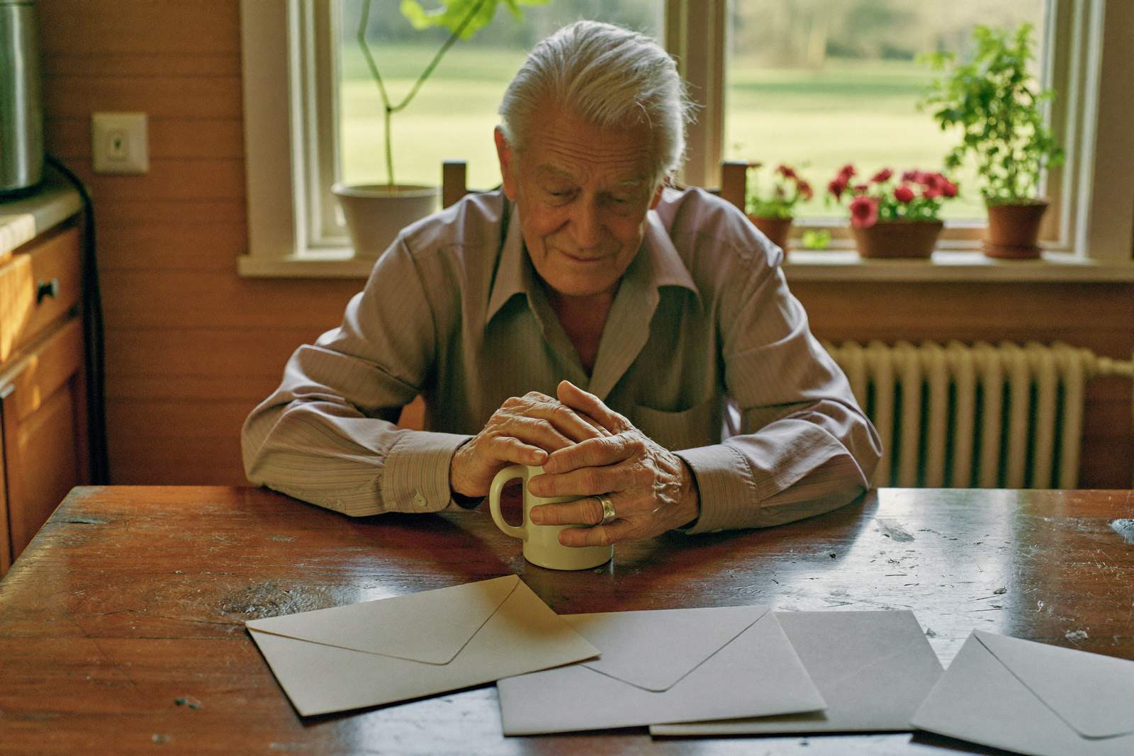Oudere man aan de keukentafel bekijkt rustig zijn post met een kop koffie